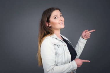 Olumlu ve çekici genç bir kadın, neşeli ve şaşkın bir ifadeyle, ağzı açık, şaşırtıcı bir şey gösterir 