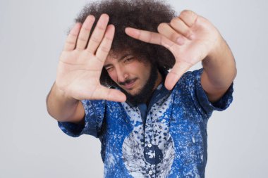 El hareketli parmak çerçevesi. Gri stüdyo duvarına yaslanırken kameraya bakıp işaret eden genç adamın portresi..