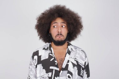 Şaşırmış genç bir adamın fotoğrafı, kıvrımlı dudaklar ve endişeli bir bakış, önünde korkunç bir şey görüyor, beyaz arka planda izole edilmiş, kot tulum giymiş..