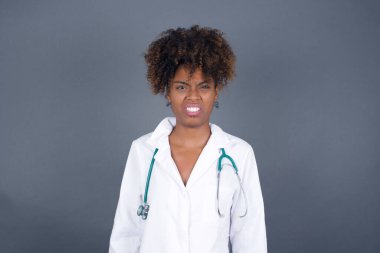 Negatif insan ifadeleri ve tavırları. Tıbbi üniforma giyen kızgın Afrikalı Amerikalı kadın doktor iğrenç bir ifade takınıyor çünkü çekici olmayan bir şey görüyor, somurtkan bir yüz, arka planda soyutlanmış. Güvensizlik ve nefret.