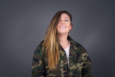 Hoş görünümlü beyaz bir kadının yatay portresi. Uzun, güzel saçlı, kahverengi kazak giyen, yüzünü saçlarıyla kaplayan ve kameraya mutlu bir şekilde bakan..