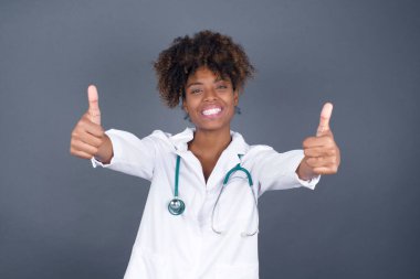 İyi iş! Afro-Amerikalı doktor kadın portresi. Kapalı alanda iki parmak hareketi yapıyor. Olumlu insani duygu yüz ifadesi vücut dili. Komik kız.