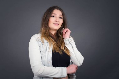Yüzüne yakın eli gri duvarda duran neşeli, güzel, beyaz bir bayan resmi. İyi haberleri dinledikten sonra kameraya mutlu bir ifadeyle bakmak. Kendine güvenen kız..