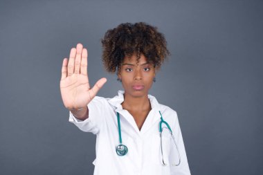 Genç Afrikalı Amerikalı doktor avucunun içi gibi jest yapıyor. Gri arkaplan üzerinde izole edilmiş yüz üzerinde negatif ve ciddi jest içeren uyarı ifadesi.