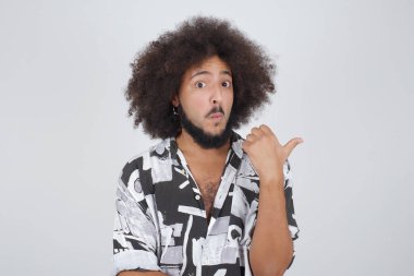 Genç ve keyifli bir erkeğin başparmağıyla yatay görüntüsü gri arkaplanda izole edilmiş boş bir duvara işaret ediyor..