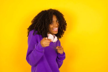 Afrika kökenli Amerikalı kadın, sarı arka planda mutlu bir ifadeyle kamerayı işaret ediyor. Duygular ve jestler konsepti