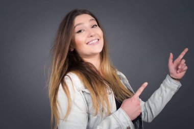 Olumlu ifadeli güzel, esmer bir kadın, sıradan giyinmiş, promosyon metnin ya da ilanın için ön parmaklarını boş fotokopi alanında gösteriyor. Sevimli kadın evde tek başına poz veriyor.