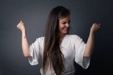 Kafkasyalı esmer kadın başarısını ve zaferini sevinçle kutluyor ve yumruklarını zevkle sıkıyor. Tüylü, şanslı kadın hedefine ve hedeflerine ulaştığına seviniyor. Olumlu duygular, duygular.