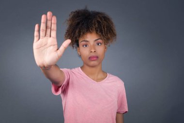 Genç, güzel, Afro-Amerikan bir kadın avuç içiyle jesti durduruyor. Gri arkaplan üzerinde izole edilmiş yüz üzerinde negatif ve ciddi jest içeren uyarı ifadesi.