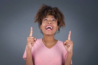 Cazibeli, güzel, afro-amerikalı, her iki işaret parmağıyla da işaret ediyor, günlük kıyafetler giymiş, geniş ilgi çekici bir gülüşü var, arka planda soyutlanmış. Şuraya bakın, lütfen.  