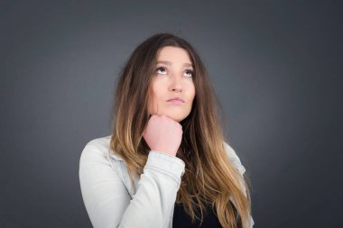 Düşünceli kadın portresi elini çenesinin altında tutuyor, bir şey hatırlamaya çalışıyor ya da ilgi çekici bir şey dinliyor, sıradan giyiniyor, içeride poz veriyor. Gençlik kavramı.