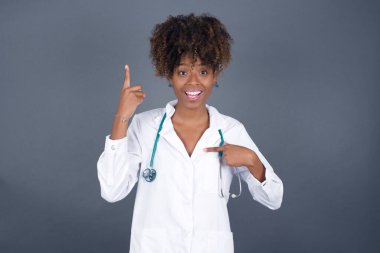 Tıbbi üniforma ve steteskop giyen Afro-Amerikan kadın doktor diyor ki: Vay be, ne kadar heyecan verici, şaşırtıcı bir ifade, bir şey ifade ediyor. Bir eli göğsünde ve diğer eliyle işaret ediyor..