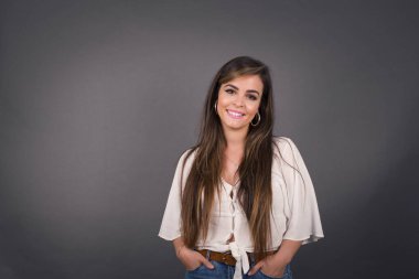 Güven ve iş kavramı. Çekici, başarılı bir genç kızın portresi. Gri duvarın önünde el ele tutuşurken kendinden emin bir ifadeyle gülümsüyor..