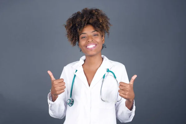 Closeup of young optimistic doctor female isolated on grey background showing thumbs up with positive emotions of content and happiness. Concept of satisfaction with quality and recommendation.