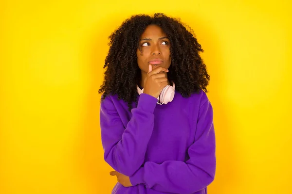 Young beautiful African American woman wearing purple knitted sweater  thinking  against yellow  background.