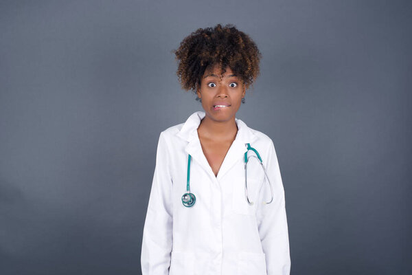  African American doctor female wearing medical uniform  nervous and scared biting lips looking camera with impatient expression, pensive 