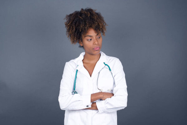Closeup portrait displeased pissed off angry African American doctor woman wearing medical uniform with bad attitude, arms crossed looking sideways. Negative human emotion facial expression feelings