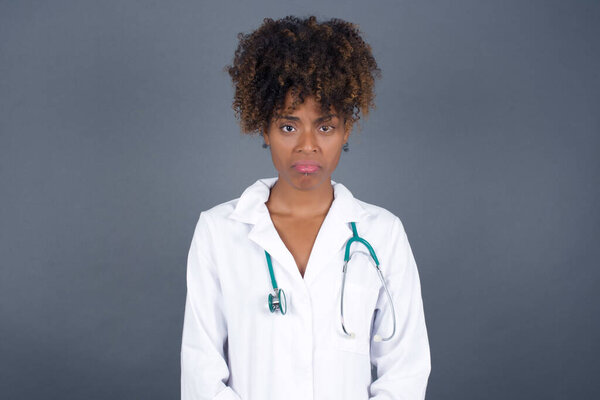 Beautiful  African American doctor female wearing medical uniform  crying desperate and depressed with tears on her eyes suffering pain and depression isolated on grey background in sadness facial expression and emotion concept.