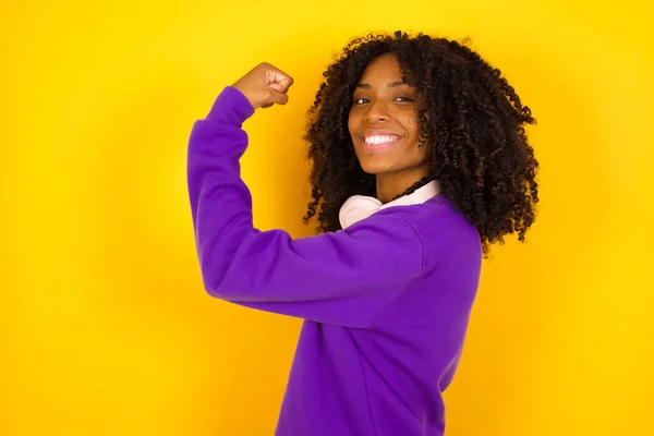 年轻美丽的非洲裔美国女人 身穿紫色针织毛衣 背对着黄色背景 显得很有肌肉 — 图库照片