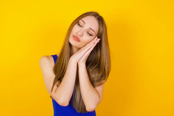 Relax and sleep time. Tired beautiful dark haired girl with closed eyes leaning on palms as pillow pretending sleeping being exhausted seeing dreams standing against gray background. Sleeping gesture.