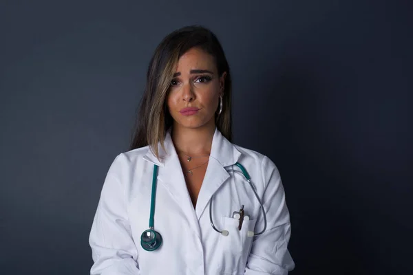 Beautiful face of sad doctor woman crying desperate and depressed with tears on her eyes suffering pain and depression isolated on grey background in sadness facial expression and emotion concept.