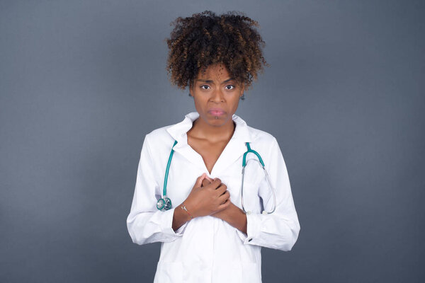 Sad African American doctor woman wearing medical uniform feeling upset while spending time at home alone. 