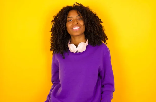 Beautiful african american woman with headphones smiling against yellow background.