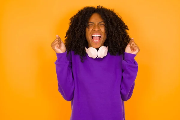 穿着紫色针织毛衣的年轻美丽的非洲裔美国女人在黄色的背景下很快乐 — 图库照片