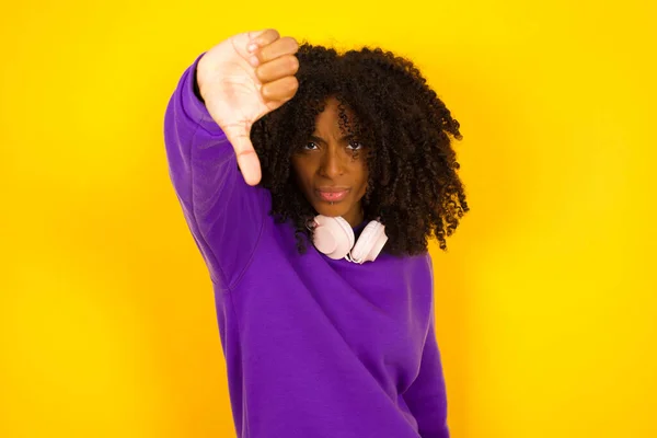 黄色の背景のアフリカ系アメリカ人女性は親指を下に示しています 感情やジェスチャーの概念 — ストック写真