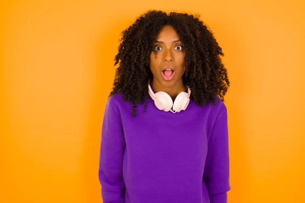 紫色の編まれたセーターを身に着けている若い美しいアフリカ系アメリカ人女性は黄色の背景と混同されます — ストック写真
