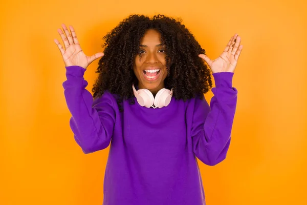 若い美しいアフリカ系アメリカ人女性は紫色の編まれたセーターを着て黄色の背景に対して手を挙げます — ストック写真