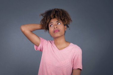 Tüh, ne yaptım ben? Genç ve güzel Afro-Amerikan kadın korkmuş ve pişmanlık dolu bir ifadeyle el ele tutuşuyor. Gri arka planda dikilen günlük giysiler giyiyor..