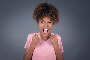 Genç ve güzel Afro-Amerikan kadın başarısını ve zaferini kutluyor yumruklarını neşeyle sıkıyor. Hedefine ve amaçlarına ulaşmaktan mutlu olan şapkalı şanslı kadın. Pozitif duygular, duygular..