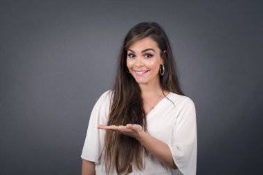 Pozitif mutlu bir kadın der ki: Vay be, ne kadar heyecan verici, hayret verici bir ifade, boş uzayda bir şey gösteriyor, açık elle izole edilmiş gri arkaplan üzerinde. Reklam kavramı.