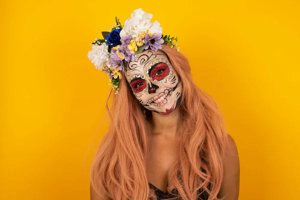 Shy girl smiling looking to the camera. Caucasian charming girl sanding against yellow studio background feeling shy.