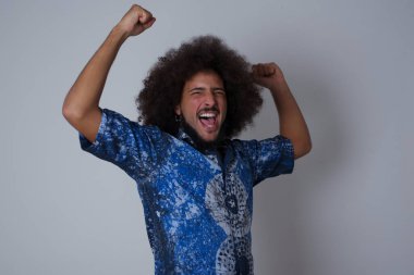 Çekici, keyifli ve heyecanlı bir adamın portresi Gri arka planda yumruklarını kaldırıyor 