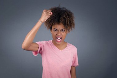 Vahşi, kendinden emin Afro-Amerikan kadın, sanki dövüşmeye ya da meydan okumaya hazırmış gibi, bağırıyor ve yüzünde agresif bir ifade var. Gri arkaplan üzerinde izole.