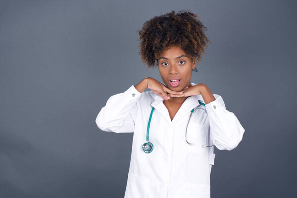 Pretty surprised african american woman doctor with hands under her chin looking playful