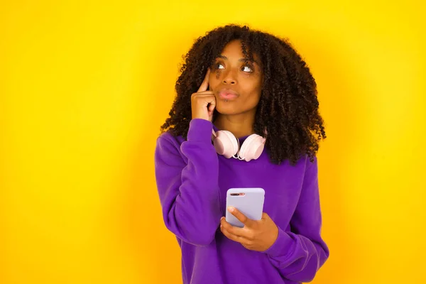 Mujer Afroamericana Sosteniendo Teléfono Pensando Algo Sobre Fondo Amarillo Concepto — Foto de Stock