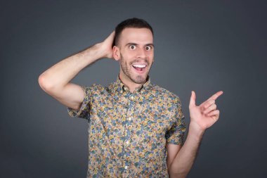 Şok olmuş yüz ifadesi olan genç bir adamın portresi, boş alanda inanılmaz bir şey gösteriyor, bir eli kafasında ve işaret parmağıyla işaret ediyor. OMG kavramı.