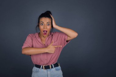 Pozitif esmer kadın bir şey gösteriyor. Bir eli kafasında, diğer eliyle işaret ediyor..