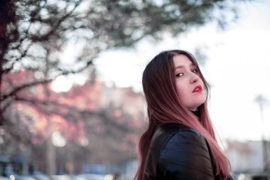 Parkta poz veren deri ceketli beyaz bir kadın.  