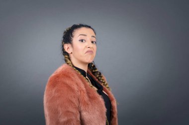 Züppe ifadeli güzel bir kadın dudaklarını kıvırıyor ve kaşlarını kaldırıyor şüpheli ve şüpheci bir ifadeyle şüpheli ve şüpheci bir ifadeyle bakıyor. Gri arka planda kapalı duruyor..