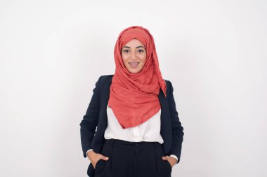 Güven ve iş kavramı. Güzel Müslüman kadının portresi, gri duvarın önünde el ele tutuşurken geniş bir tebessüm ile gülümseyen siyah ceket ve başörtüsü giyer..