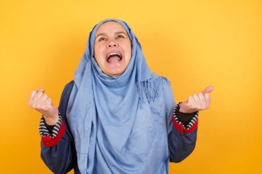 Güzel, orta yaşlı, tesettürlü Müslüman kadın portresi heyecanla bakıyor, ellerini havada tutuyor, beklenmedik bir şey fark ediyor, içeride poz veriyor. Güzel bir kadın ani haberlere tepki verir..