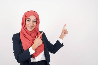 Reklam konsepti. Pozitif, güzel Müslüman kadın siyah ceket giyiyor ve arka planda tesettür iki işaret parmağıyla işaret ediyor ve boş kopya alanına bakıyor.