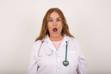 Etkileyici yüz ifadeleri. Kafkasyalı doktor üniformalı kadın, boş gri duvarda gördüklerinden sersemledi.