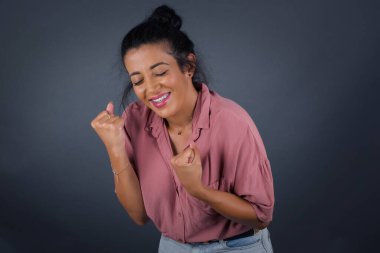 Kafkasyalı esmer kadın başarısını ve zaferini sevinçle kutluyor ve yumruklarını zevkle sıkıyor. Saçları topuzlu şanslı kadın hedefine ve hedeflerine ulaştığına seviniyor..