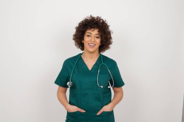 Güven ve iş kavramı. Çekici, başarılı genç doktor kadın portresi, ceplerinde el ele tutuşurken kendinden emin bir ifadeyle gülümsüyor..