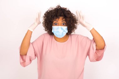 Yüz maskesi takan ve günlük giysiler giyen bir kadın beyaz stüdyo arka planında yalnız kalmaktan korkuyor.